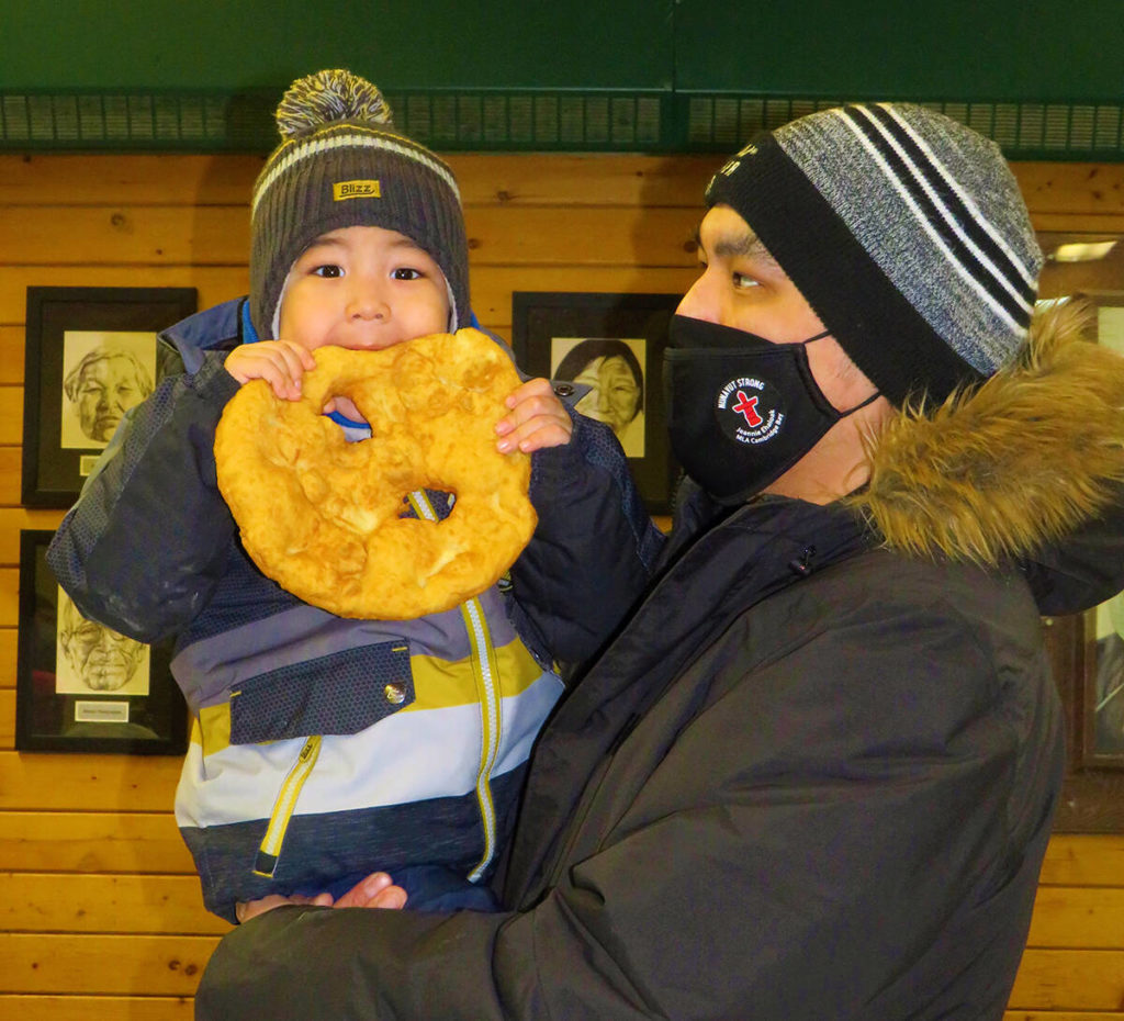 Look Mom! I love bannock! Here is 2-year-old Damian Mitkoenik Matomiak and his dad Damian enjoying fresh bannock at the Christmas Bazaar held Nov. 13. Navalik Tologanak/NNSL photoᐊᓈᓇ ᑕᑯᒍᒃ ! ᐸᓚᐅᒑᖅ ᒪᒪᕆᔮᓗᒐ ! ᐅᓇ ᒪᕐᕉᖕᓂ - ᐅᑭᐅᓕᒃ ᑕᐃᒥᐊᓐ ᒥᑦᑯᐃᓐᓂᖅ ᒪᑐᒥᐊᒃ ᐊᒻᒪ, ᐊᑖᑕᖓ ᑕᐃᒥᐊᓐ ᒪᒪᑕᒃᑐᑦ ᐸᓚᐅᒑᓕᐊᒥᒃ ᖁᕕᐊᓱᒡᕕᖕᒥ ᓂᐅᕕᕋᕐᔪᐊᕐᓂᐅᔪᒥ ᐱᓕᕆᐊᖑᓚᐅᖅᑐᒥ ᓄᕕᐱᕆ 13 –ᒥ .