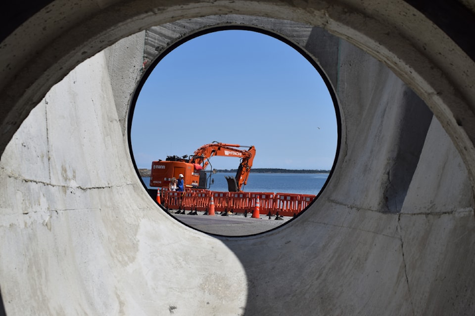 An excavator parked on Willows Beach, seen through concrete piping.