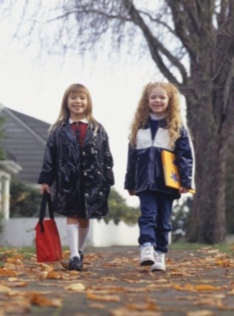 Two schoolgirls (6-7) walking side by side on sidewalk