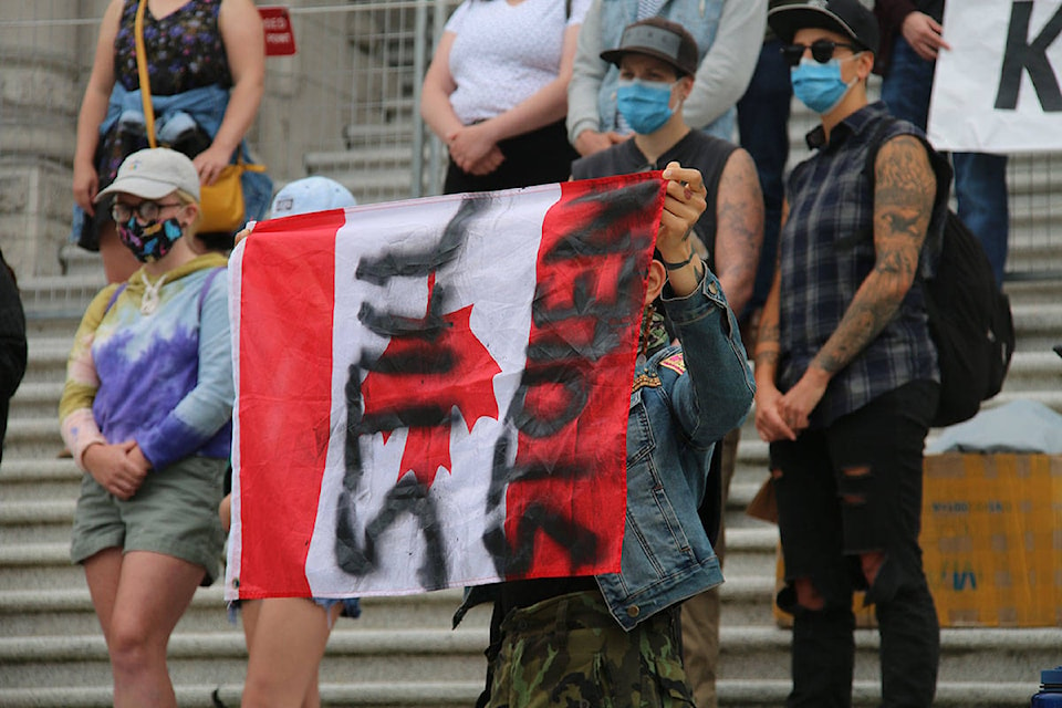 A person standing on the Legislature steps as part of the Resist Canada 153 rally, holds a Canadian flag with the words ‘still stolen’ painted on it. (Kendra Crighton/News Staff)