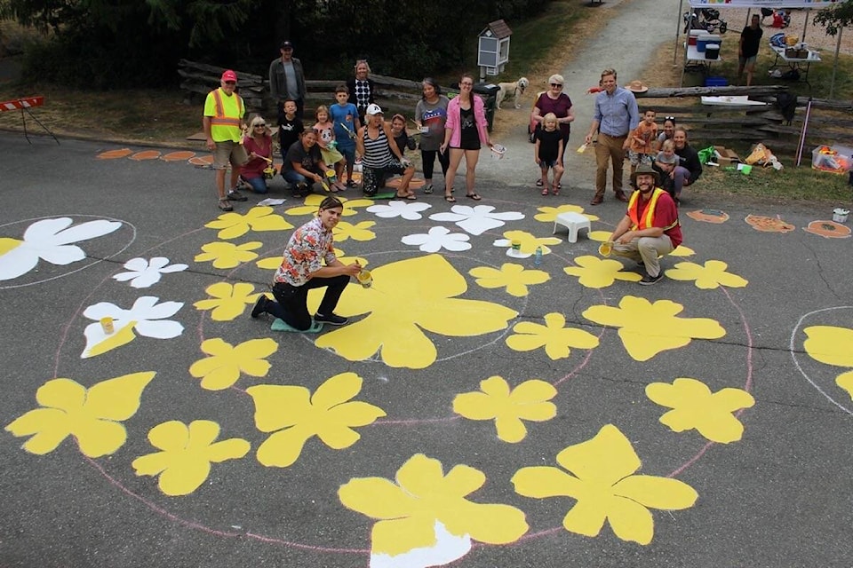Volunteers and neighbours gather around the road mural in progress near the entrance of Falaise Park in Saanich. (Austin Westphal/News Staff)