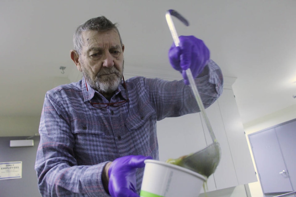 Richard Waller ladles soup into containers for diners to take away with the recently implemented bag lunch program at The Soup Kitchen in Victoria. (Christine van Reeuwyk/News Staff)