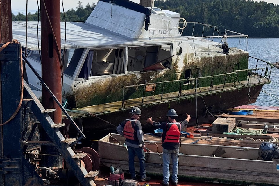 Two crew members on the barge in front of the derelict boat.
