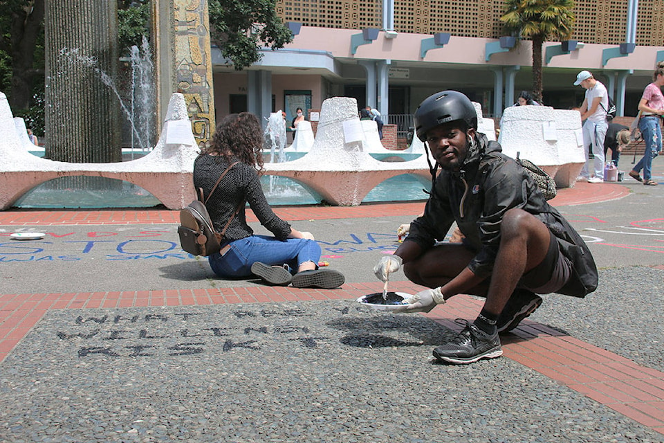 Liam Kenah paints ‘what are you willing to risk?’ on the ground in Centennial Square, helping to rebuild the display that was destroyed earlier in the week. (Kendra Crighton/News Staff)