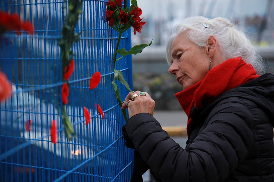 Victoria residents pin poppies and flowers to the fence surrounding the Victoria cenotaph on Remembrance Day 2020. (Jane Skrypnek/News Staff)
