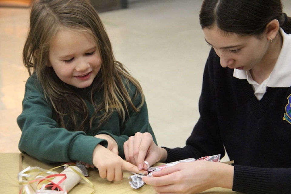 Kindergartener Lucille McKenzie and her Grade 7 buddy Eliza Gedischk build tiny bundles of candy with a warm message during the years-old tradition of Christmas Cracker Day at St. Patrick’s School. (Christine van Reeuwyk/News Staff)