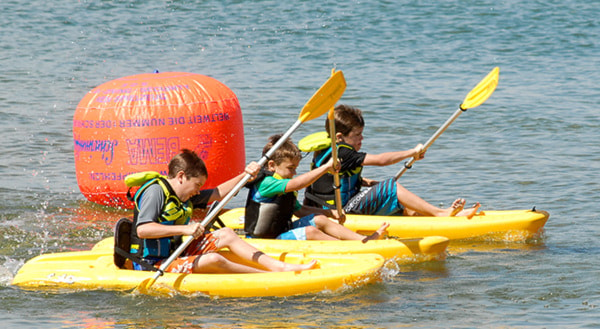 Evan, Eric and Cameron Miller dig in with their paddles as they race minikayaks at the Peachfest Regatta Saturday, sponsored by Hoodoo Adventures. Steve Kidd/Western News Staf
