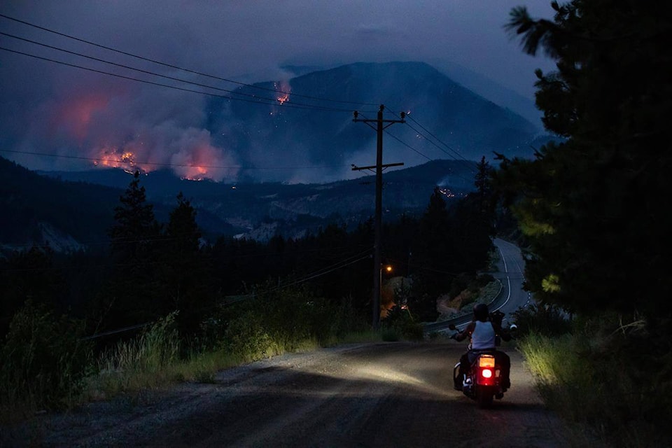A man rides off on his motorcycle after stopping to watch a wildfire burn on the side of a mountain in Lytton, B.C., Thursday, July 1, 2021. Experts in wildfires and fire ecology say British Columbia must spark far more prescribed burns, akin to how Indigenous communities have managed forests, to mitigate the risk of huge, destructive blazes the province has seen in recent years. THE CANADIAN PRESS/Darryl Dyck