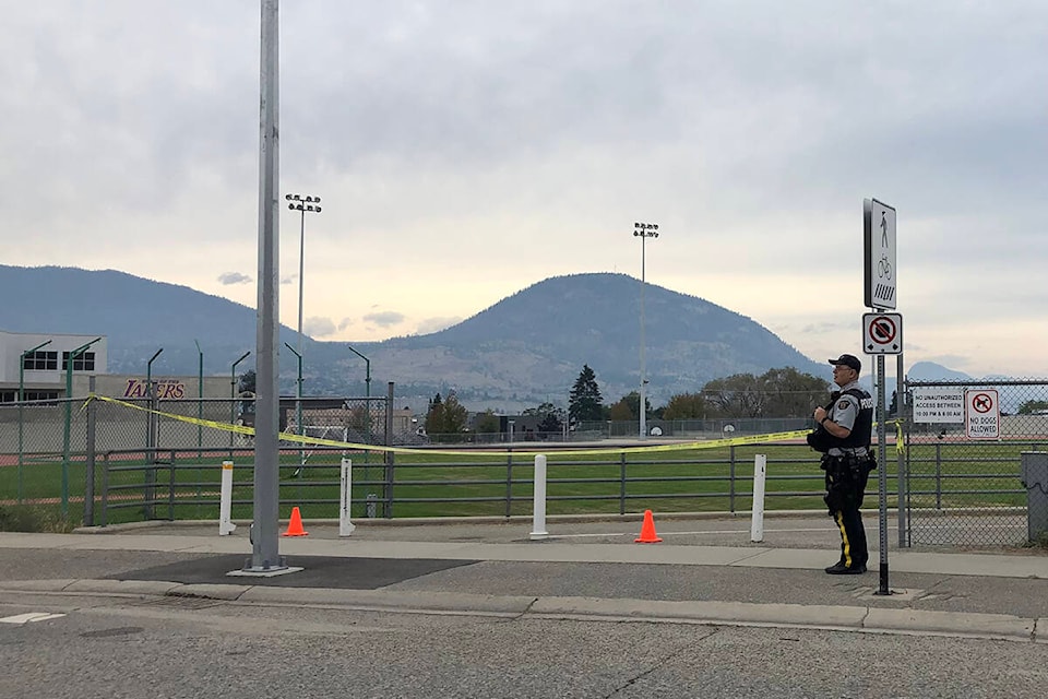 A Penticton RCMP officer stands at the police tape blocking off the track and field behind Penticton High School Sunday afternoon where the body of a young man was found. (Monique Tamminga Western News)