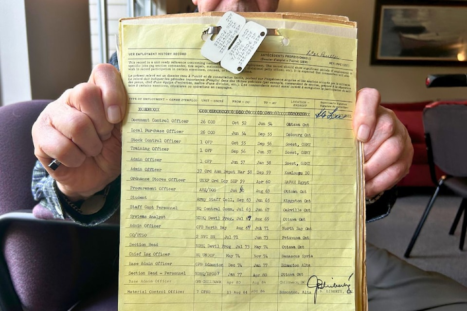 Veteran Jack Poulter holds up his unit employment record, which shows his military career and placements. His metal identification disks are tagged to the top