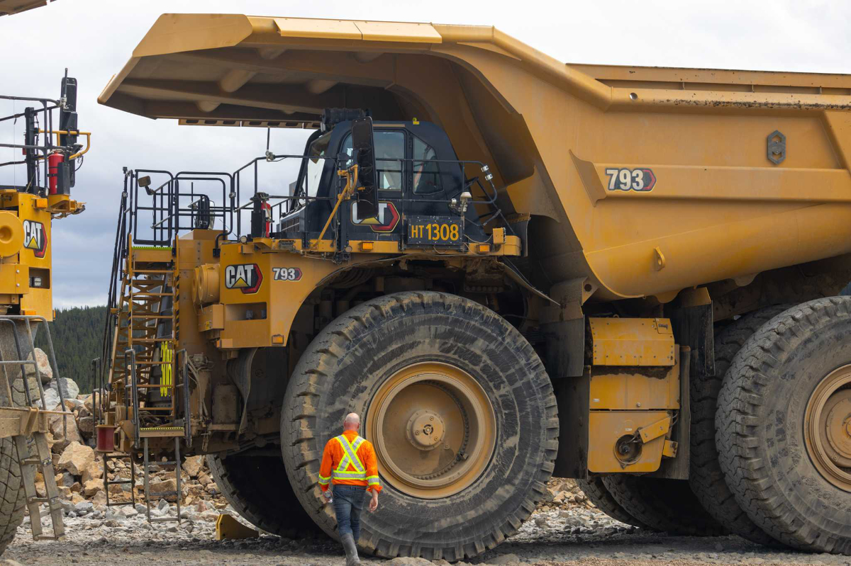 A hauler truck, massive in size as a man walks towards it, showing its scale.