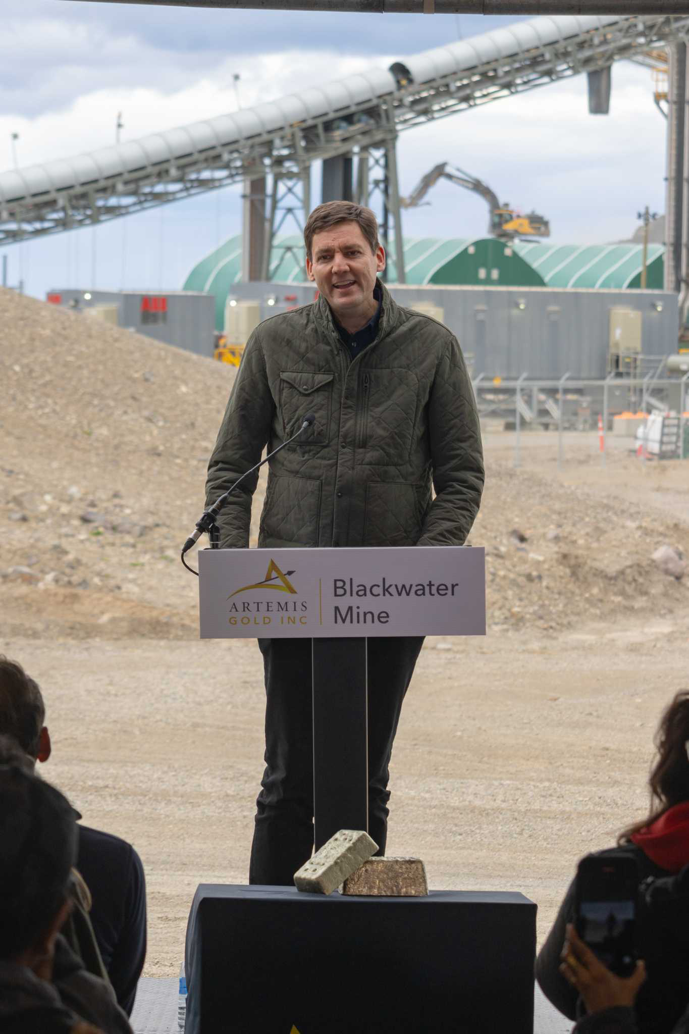 David Eby stands at a podium in front of large gold and silver bars