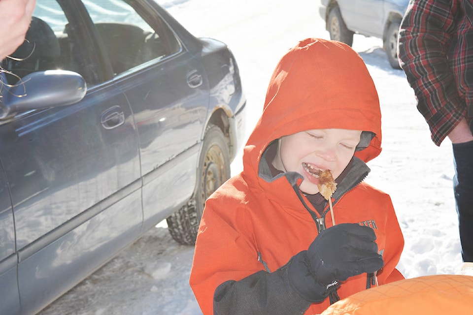 Four-year-old Riley Cartier (left) and six-year-old Liam Cartier try maple syrup on snow during the third annual Festival du Sucre and National Flag Day Monday at the Bouchie Lake Country Store. The festival included games, a Canada flag parade and a variety of Canadian treats, including tarte au sucre, beavertails and tourtiere. Lindsay Chung photo