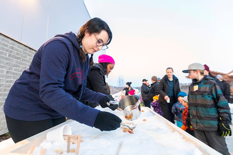 Sarah Thompson and Jadacia Barker pour some hot maple syrup over snow to create sweet treats for patrons of the Boots and Toques event at the West Fraser Centre on Feb. 22. (Sasha Sefter - Quesnel Cariboo Observer)