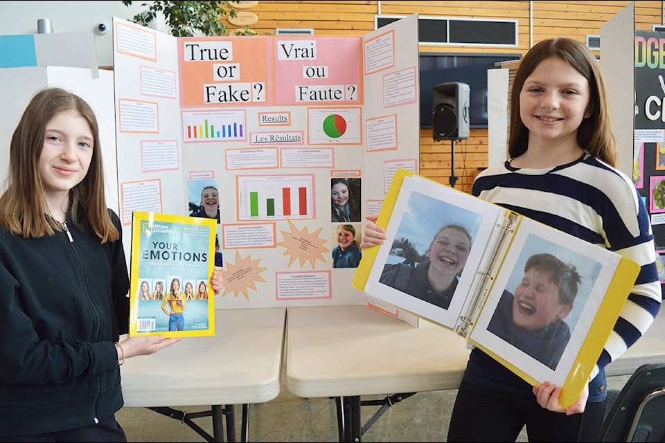 Aubrey Williams, (left) and Rome Borsato-Stobbe, who are in Grade 6 at École Red Bluff Lhtako Elementary, present their science fair project at the School District 28 fair, held Friday, Feb. 21 during Science and Technology Day at the College of New Caledonia Quesnel Campus. Williams and Borsato-Stobbe wondered if people could recognize true emotion or not, and they had people look at 10 photos of people showing happiness and guess if they were real or fake. On average, people guessed correctly six out of 10 times. They also tested the Duchenne smile theory, which involves smiling with your whole face, and found that volunteers identified true smiles 70 per cent of the time. (Lindsay Chung - Quesnel Cariboo Observer)