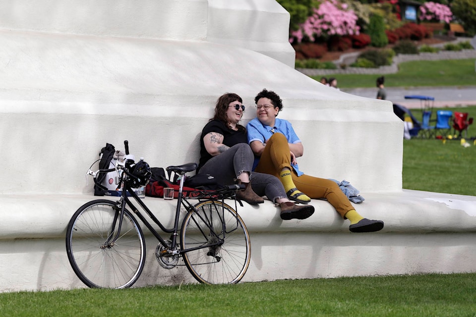 In this photo taken May 17, 2020, sweethearts Hannah Smith, left, of Vancouver, British Columbia, and Jabree Robinson, of Bellingham, Wash., sit on the base of the Peace Arch as they visit at the border between Canada and the U.S. at Peace Arch Park, in Blaine, Wash. With the border closed to nonessential travel amid the global pandemic, families and couples across the continent have found themselves cut off from loved ones on the other side. But the recent reopening of Peace Arch Park, which spans from Blaine into Surrey, British Columbia, at the far western end of the 3,987-mile contiguous border, has given at least a few separated parents, siblings, lovers and friends a rare chance for some better-than-Skype visits. (AP Photo/Elaine Thompson)