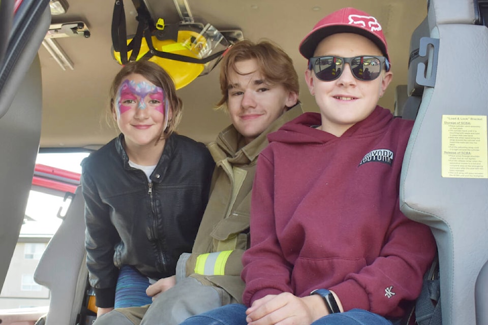 Firefighter Evan Arthur (centre) attended the parking lot party with his siblings Emma (left) and Riley (right). Arthur who is just 16 years old joined the Kersley Volunteer Fire Department earlier this year as a way of giving back to his community. (Rebecca Dyok photo — Quesnel Observer)