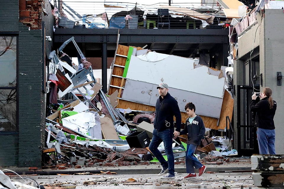 People walk past buildings damaged by storms Tuesday, March 3, 2020, in Nashville, Tenn. Tornadoes ripped across Tennessee early Tuesday, shredding buildings and killing multiple people. (AP Photo/Mark Humphrey)
