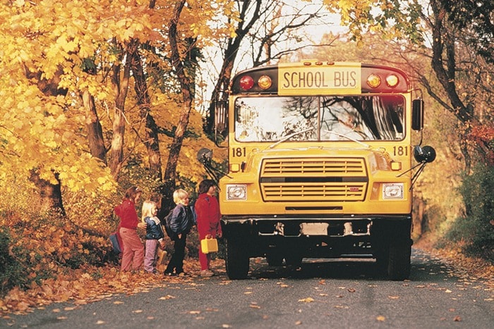 Children boarding school bus on rural road in autumn