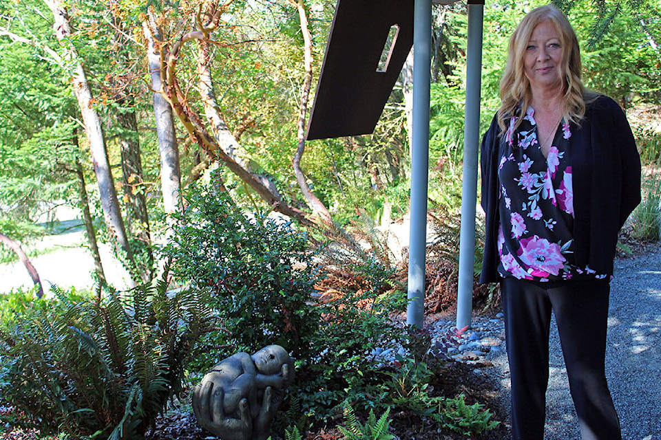 Lorraine Fracy, manager of business development and client services for the Royal Oak Burial Park, stands with a newly implemented statue in the Little Spirits Garden – one that is both raw and captures a mother’s love, she said. (Megan Atkins-Baker/News Staff)