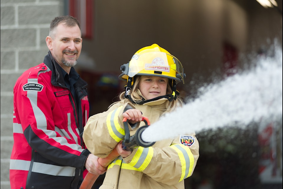 Lt. Tyler Stevenson assists Bastion Elementary student Zosia Cichosz on a fire hose during the Salmon Arm Fire Department's Fire Chief for a Day event on Wednesday, Oct. 30, 2024. 