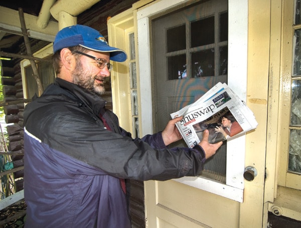 Chris Pretty delivers a newspaper to the front door of a house along his route.