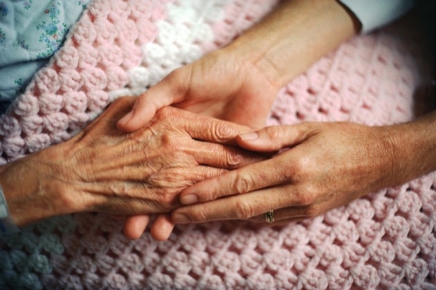 A geriatrician holds the hand of an elderly woman with arthritis