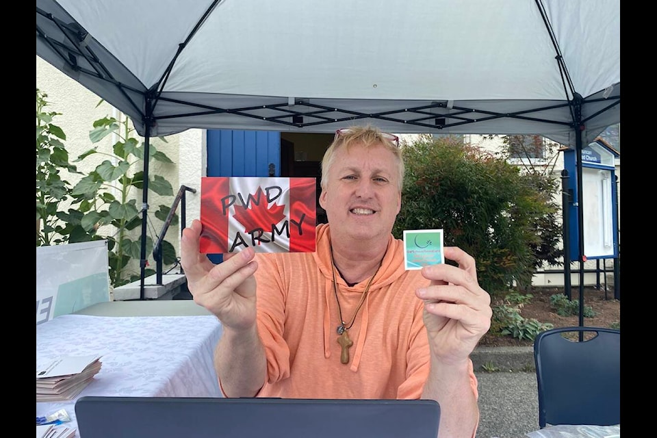 Disability advocate Jeff Leggat of Duncan holds up a postcard which will be mailed to Prime Minister Trudeau, and a temporary tattoo in his efforts to raise awareness about the legislated poverty in Canada and to see it end. Leggat had his booth set up in front of Duncan United Church on Sept. 6 before embarking on his Western Canada tour from Sept. 7 to 16. (Chadd Cawson/Citizen) 