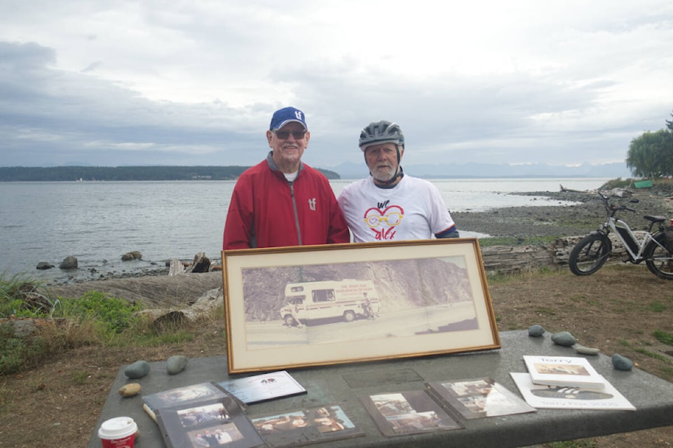 Doug Vater, left, and Bruce Lamont take a picture in front of Vater’s picture of the Marathon of Hope caravan. Vater drove in the van with Terry Fox during his attempt to run across Canada in 1980. Photo by Edward Hitchins/Campbell River Mirror 