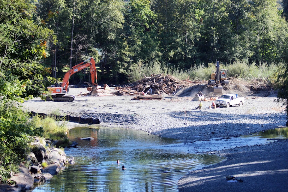 Workers with heavy equipment clear build-up at gravel bars along the Chemainus River while two people take an unseasonable swim in the river. (Photo by Don Bodger) 