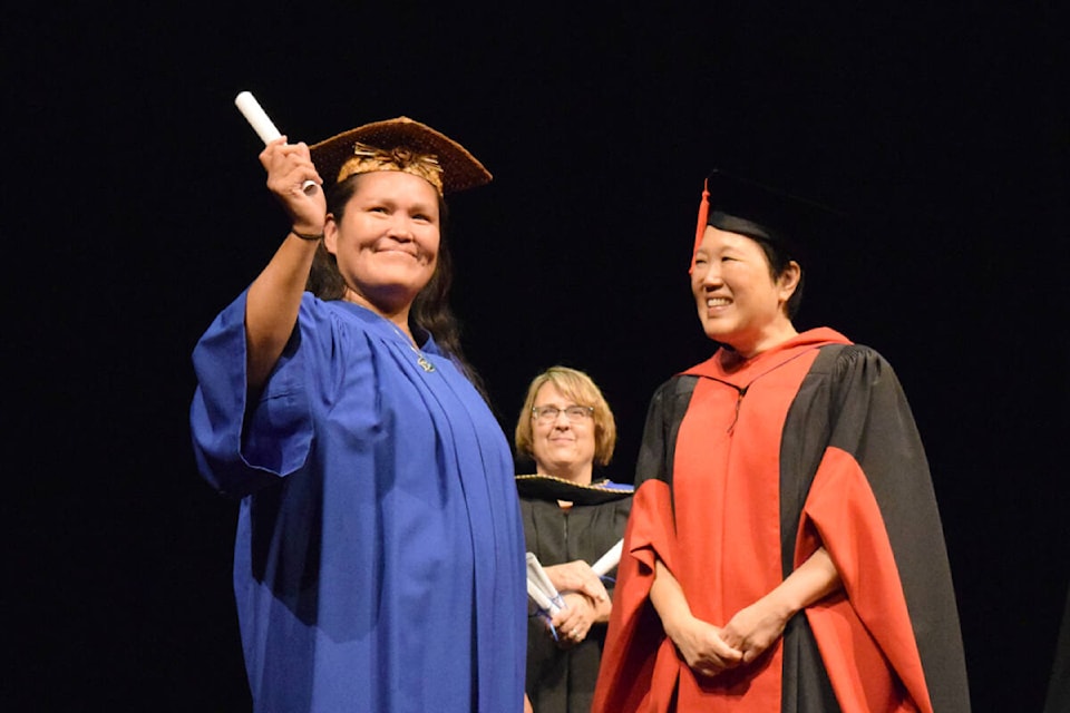 A graduate from North Island College’s Indigenous Studies Department waves to the crowd after receiving a certificate from NIC president Lisa Domae. (ELENA RARDON / Alberni Valley News) 