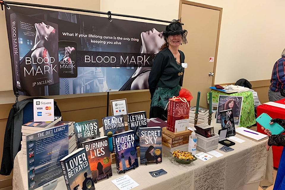 J P McLean, award-winning author, posing with a collection of her novels at Bookfest 2022. Photo by Mary Catherin Rolston 