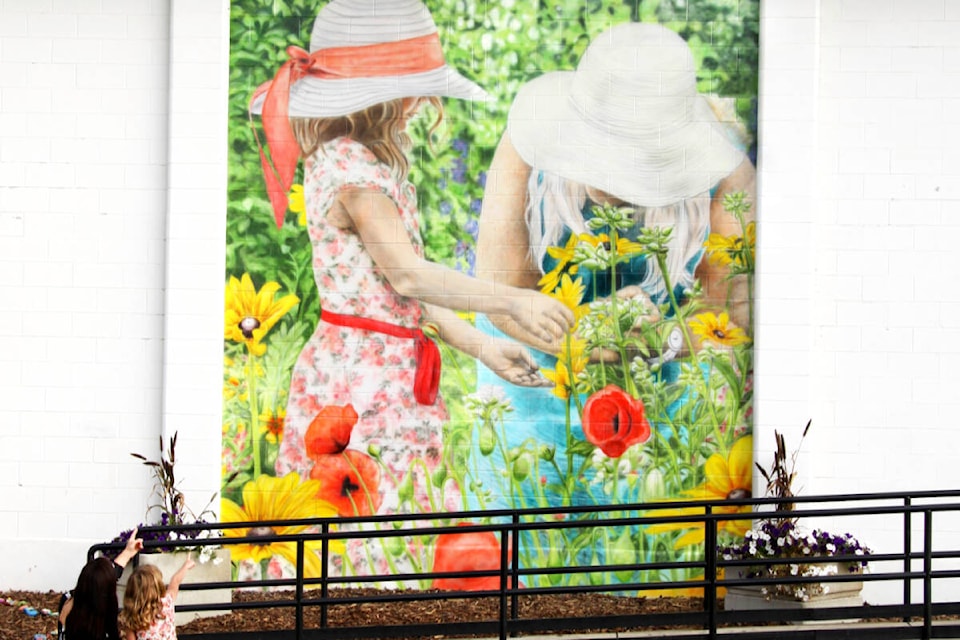 Muralist Renee Audy’s I AM Community towers on the side of the community hall in Millet, Alta. and depicts a five-year-old girl and a retired school teacher from the community, counting, smelling and playing with flowers in a local wildflower garden. (Courtesy Renee Audy) 