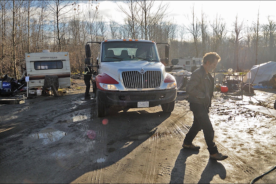 A resident of a homeless encampment at Island 22 walks past a tow truck on Friday, Dec. 8, 2023. The encampment is on lands owned by Shxwhá:y Village. (Jenna Hauck/ Chilliwack Progress) 