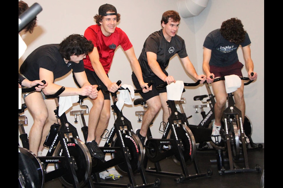 100 Mile House Wrangler Trent Thiessen, in red, and Ethan Hofstrand, in grey, laugh as they take part in a spin class last month. (Patrick Davies photo - 100 Mile Free Press) 