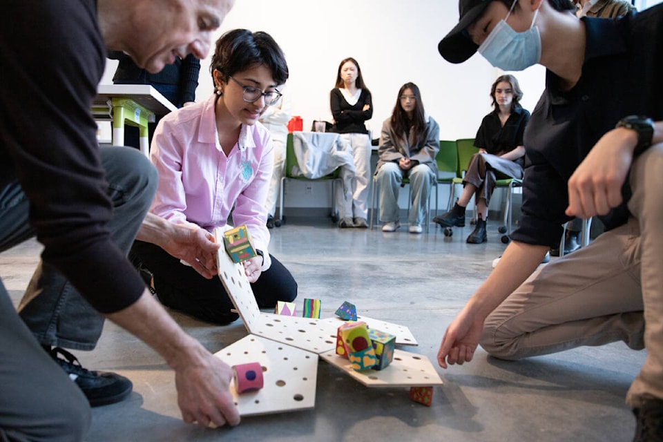 Designer and Emily Carr professor Christian Blyt (left) and design students Saanvi Bhat (centre) and Tai Vo (right) test out a final prototype interactive object for children living with trauma, created by Saanvi and Tai with classmate Joey Kim. Their design allows kids to piece together six pentagons in different formations and then place colourful blocks in holes drilled into the base. (Perrin Grauer/Emily Carr University) 