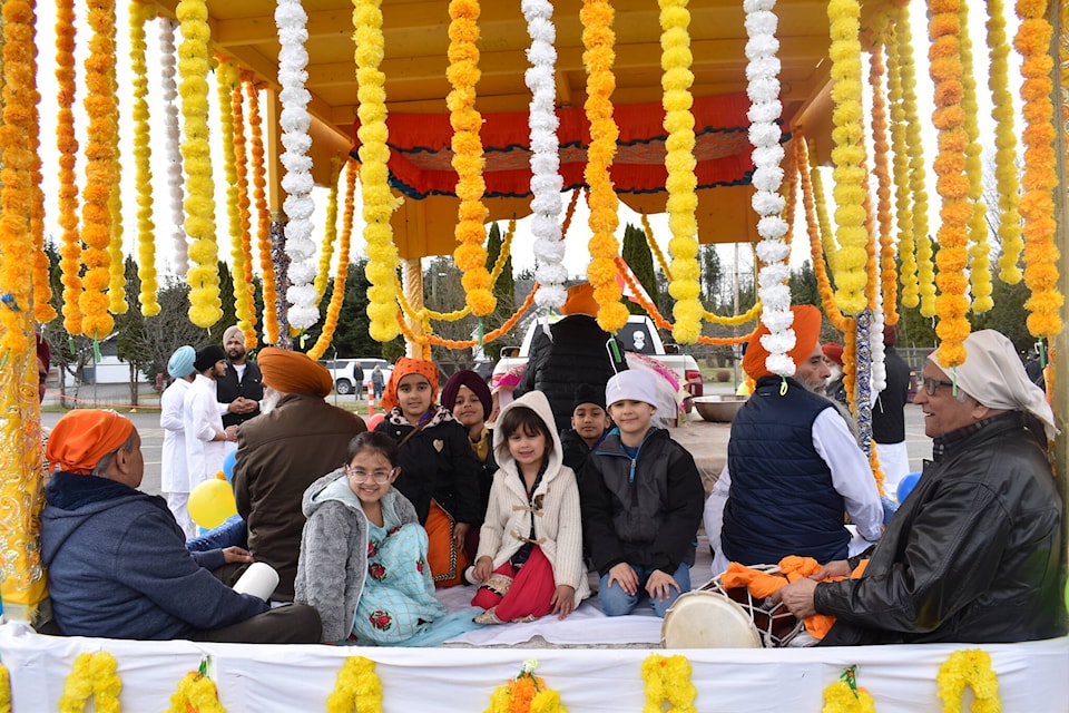 Children smile at the camera as they sit in the decorated float carrying the Sikh holy book, Guru Granth Sahib Ji during the Vaisakhi and Khalsa Day procession in Terrace on Saturday April 13, 2024. (Prabhnoor Kaur/ The Terrace Standard) 