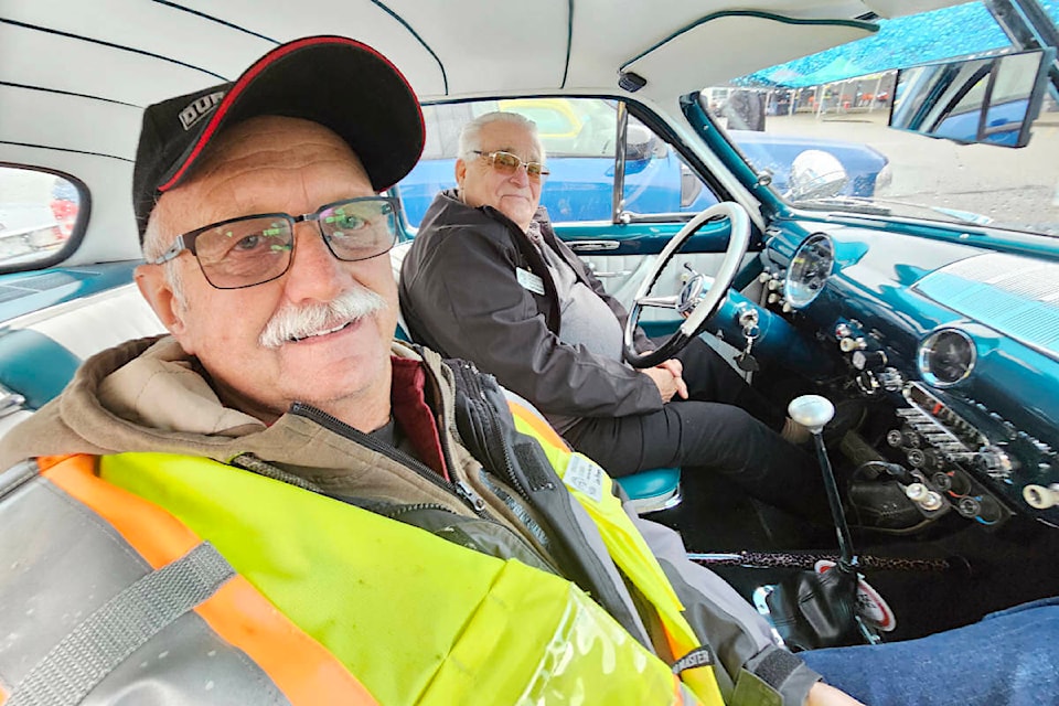 Aldergrove’s Leo Ferraro (foreground), one of the volunteers at the 10th annual Country Car Show in the parking lot of the Aldergrove Community Secondary School, took temporary shelter from the rain inside a classic 1950 Ford owned by Chilliwack’s Gordon Stebanuk (at the wheel), one of several classic and cool vehicles on display on Sunday, April 28. (Dan Ferguson/Langley Advance Times) 