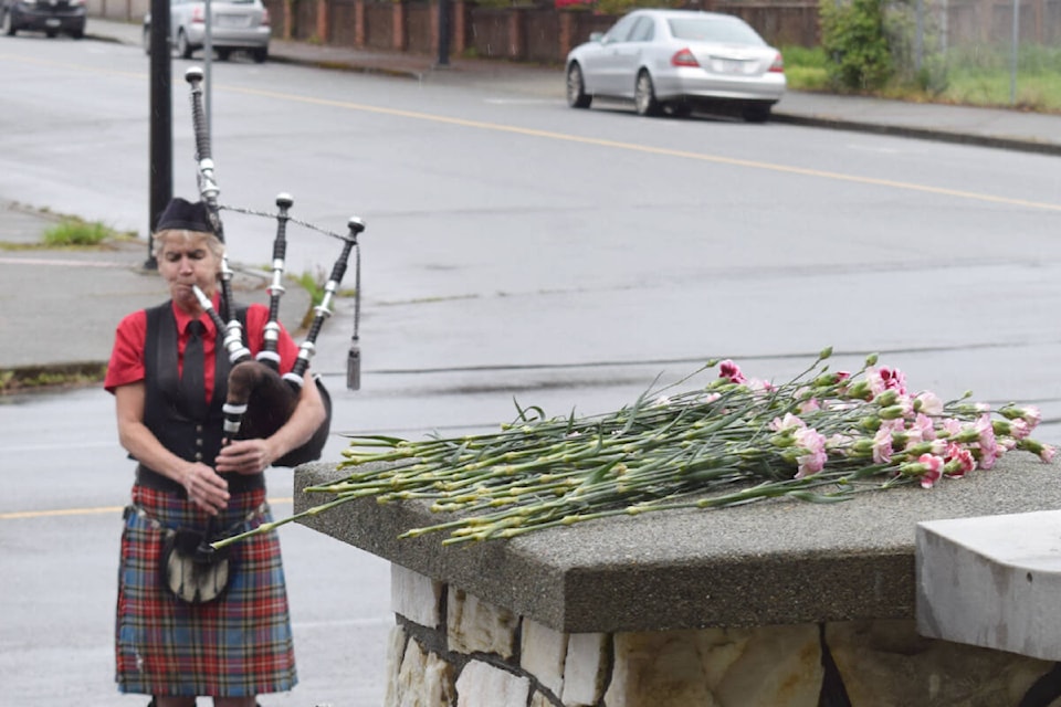 Piper Del Linden plays behind the cenotaph at the United Steelworkers Hall, where people have laid carnations to mark the Day of Mourning. (ELENA RARDON / Alberni Valley News) 