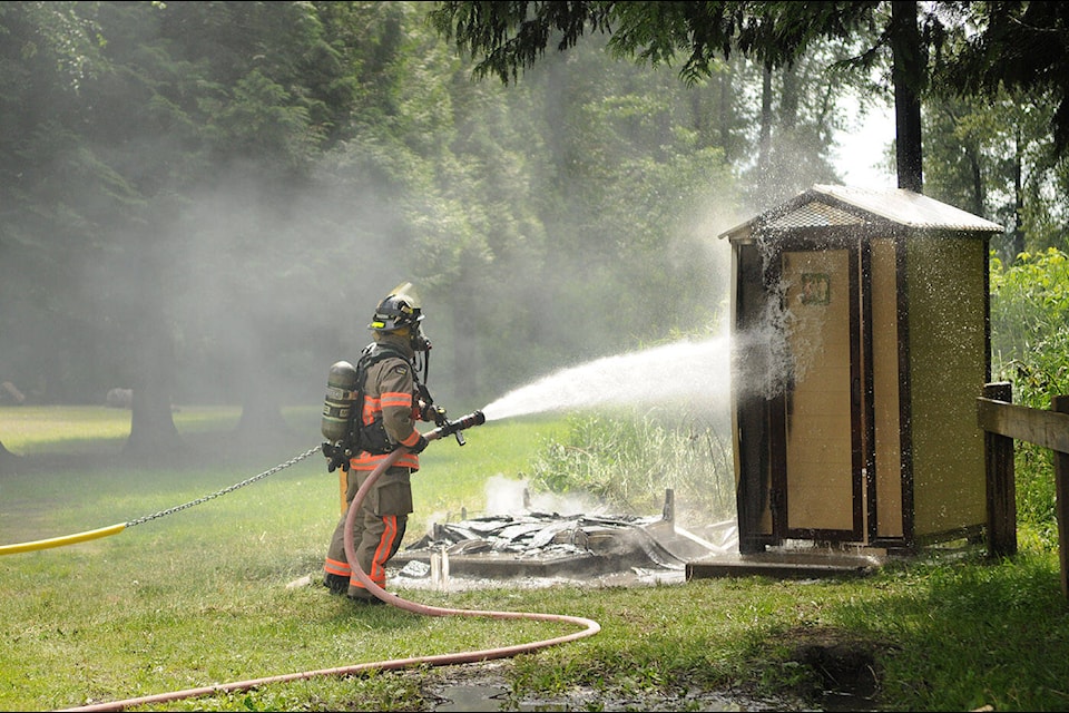 A firefighter extinguishes a blaze in an outhouse while another is seen burnt to the ground at Island 22 in Chilliwack on Wednesday, May 22, 2024. (Jenna Hauck/ Chilliwack Progress) 