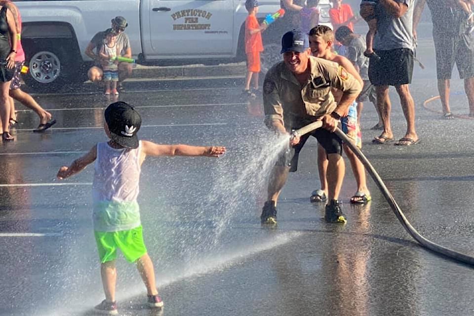 A Penticton firefighter sprays down a child at the Hot Nights water fight in the parking lot of the South Okanagan Events Centre June 28, during the heat dome. (Alysha Jacobs photo) 