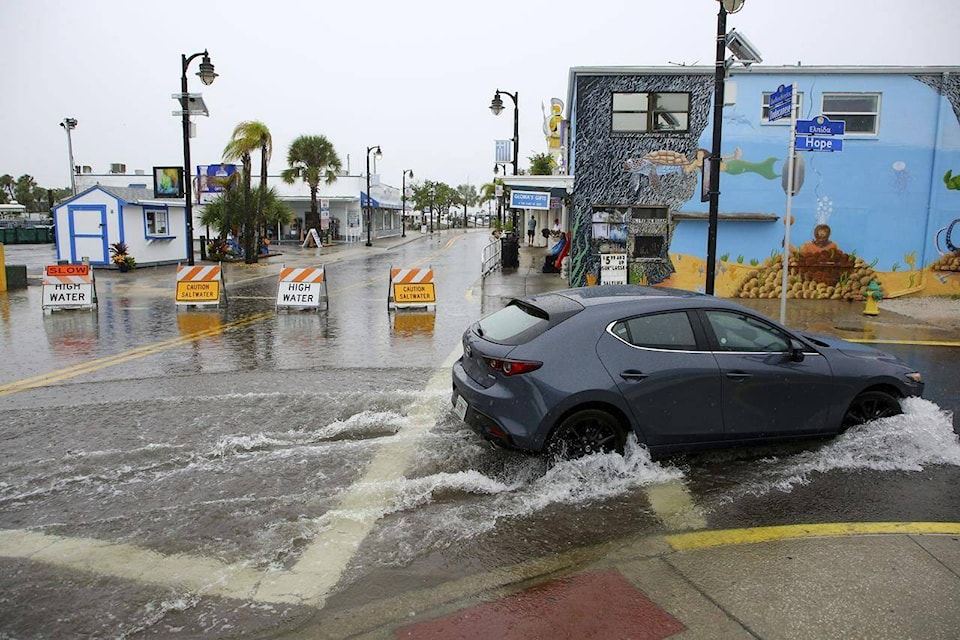 Visitors to the Tarpon Springs Sponge Docks navigate a flooded street on Sunday, Aug 4, 2024 in Tarpon Springs, Fla., as Tropical Storm Debby stirs moisture offshore in the Gulf of Mexico. (Douglas R. Clifford/Tampa Bay Times via AP) 