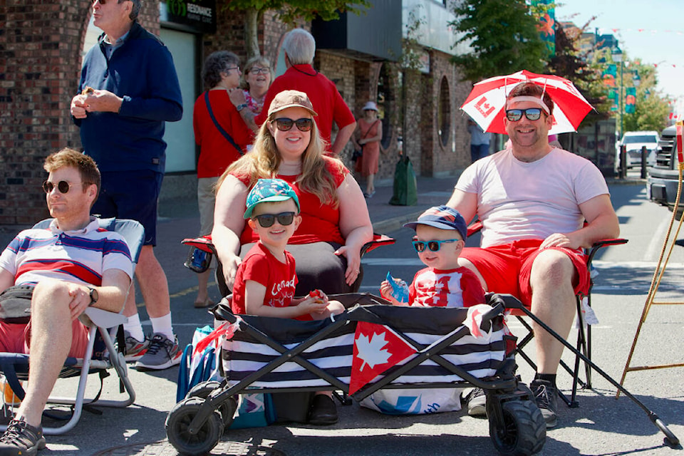 A family dressed in Canada Day garb sits along Beacon Avenue Friday to take in Sidney’s Canada Day Parade. The parade returned in person after a two years due to the pandemic. (Justin Samanski-Langille/News Staff)
