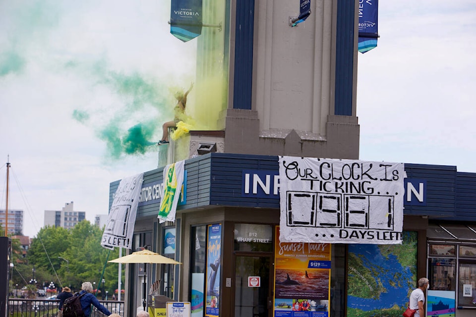 A Save Old Growth supporter sits on the roof of the Victoria Visitor centre with coloured smoke Aug. 9 during a demonstration. (Justin Samanski-Langille/News Staff)