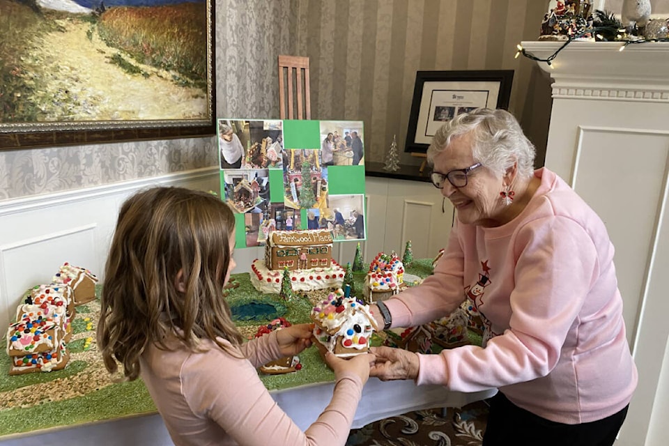 Shirley Lou Hansen, a resident of Parkwood Place, helps a student place her gingerbread house in the village. (Courtesy of Cheryl Chalifour)