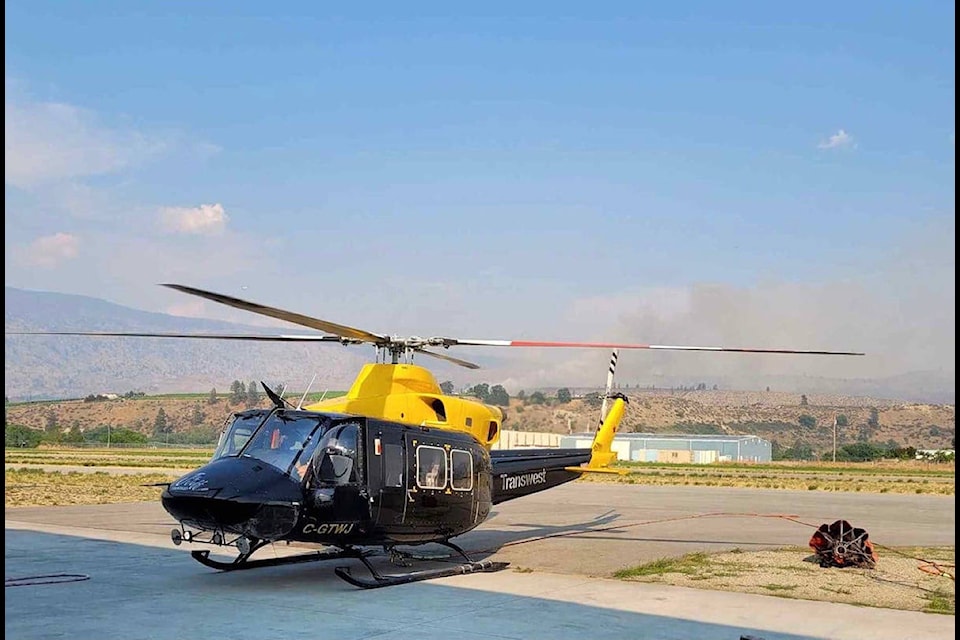 Transwest Helicopters is using Oliver Airport as its base to help fight local wildfires, including the Oliver fire that broke out July 4, 2021 and can be seen in this picture behind the helicopter. (Transwest photo)