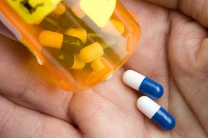 closeup of medicine capsules being poured from pill bottle into hand