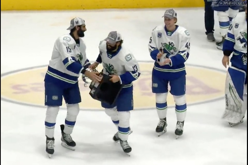 Abbotsford Canucks forward Jujhar Khaira, left, passes the Calder Cup to teammate Arshdeep Bains at Bojangles Coliseum in Charlotte, North Carolina, on June 23, 2025.