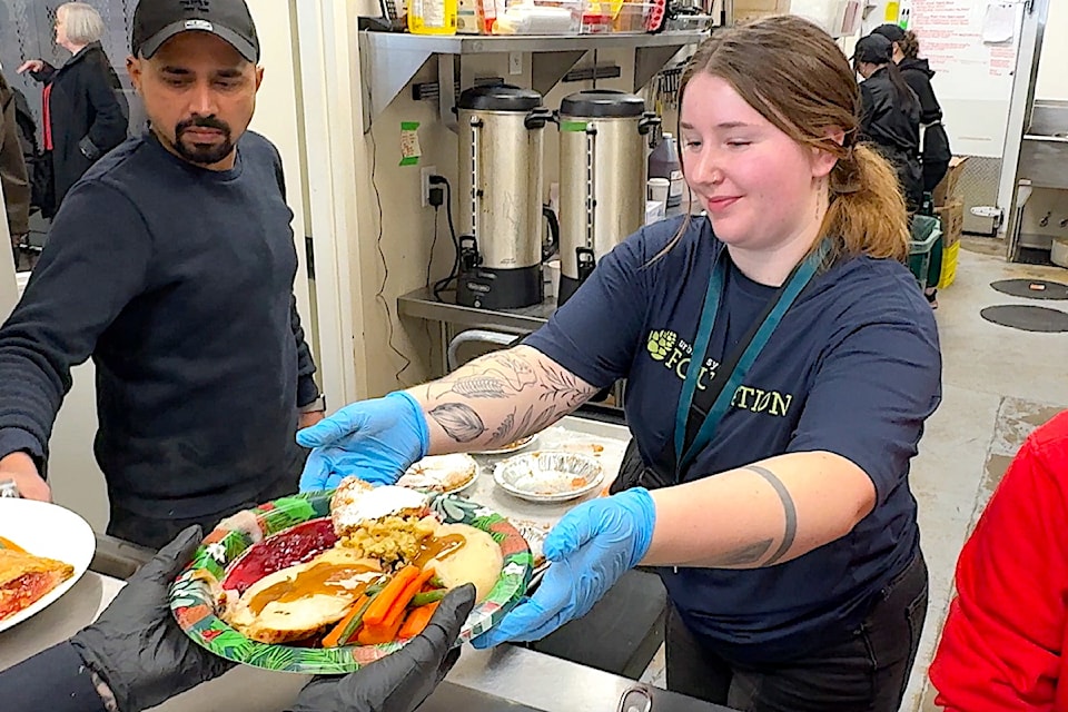Volunteer Zoe Scattergood, an employee with Urban Systems community consulting firm, serves a plate of turkey and trimmings during a holiday lunch at Surrey Urban Mission's Welcome Hub facility on Thursday, Dec. 5, 2024, at 13545 King George Blvd., Surrey. 