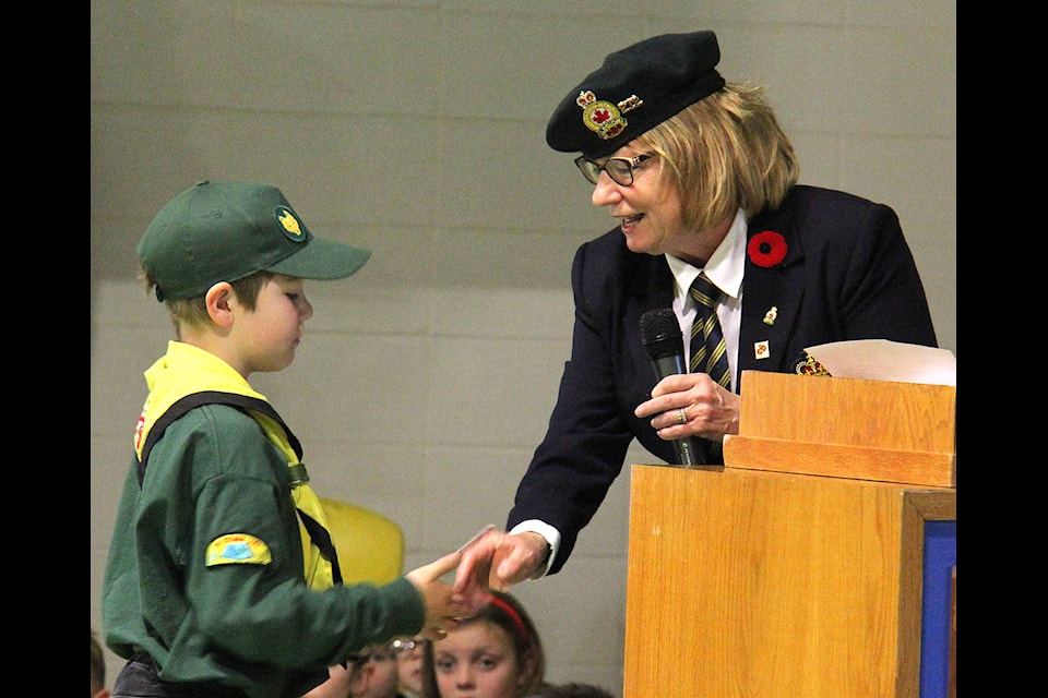 Dressed in his Scout uniform Noah Kangas receives a postcard from Normandy presented by Legion Member Patricia Gravik at Ecole Our Lady of the Rosary’s Remembrance Day service on Nov. 7. Gravik spoke to the assembly of students, teachers and parents about her recent trip to Normandy, France. Photos by Megan Roth/Sylvan Lake News